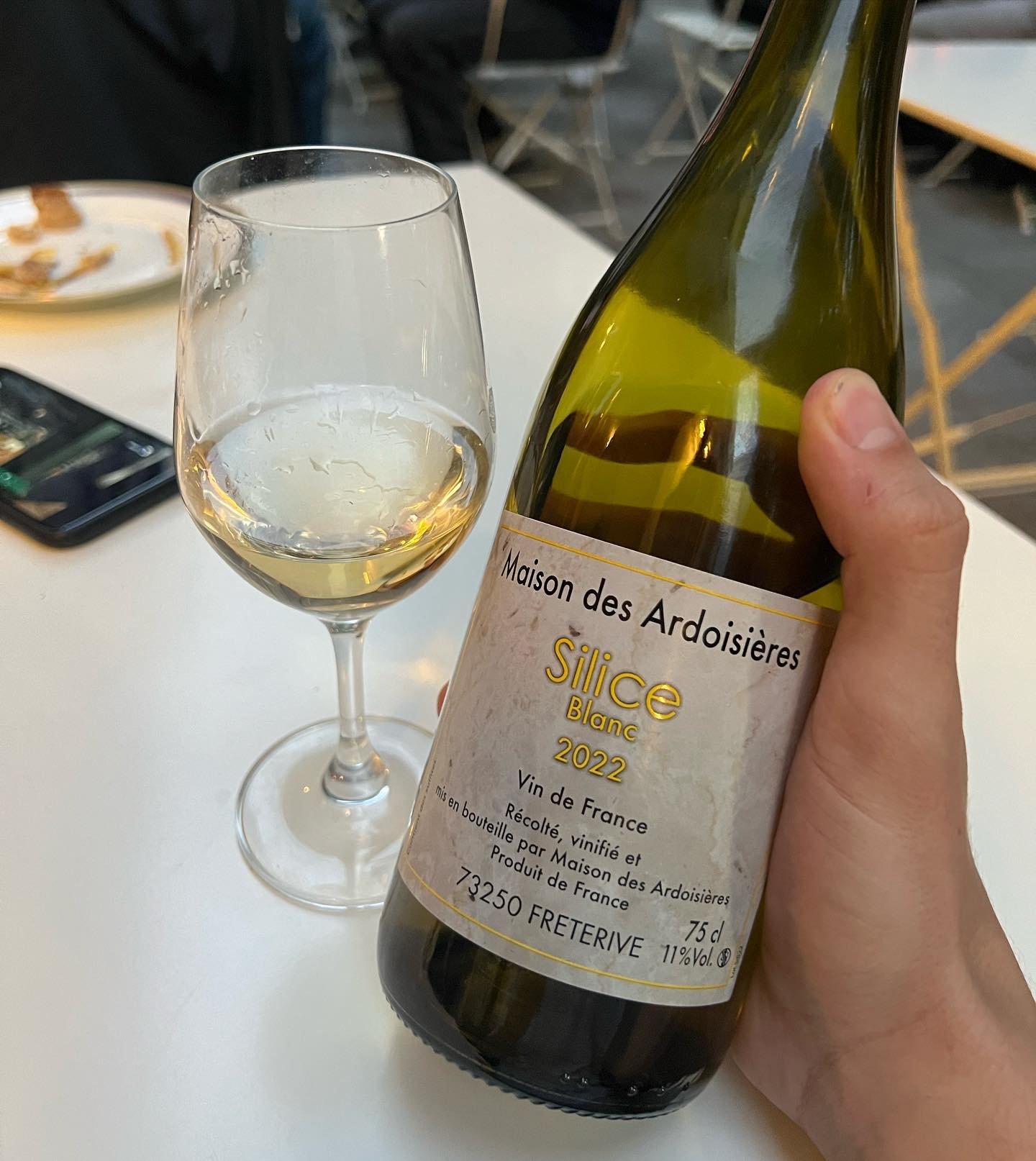 A hand holding a wine bottle beside a poured glass of white wine